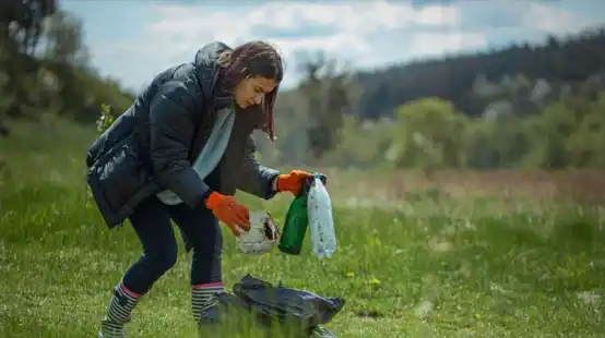 A woman diligently cleans up litter in a field, demonstrating easy ways to keep the environment clean